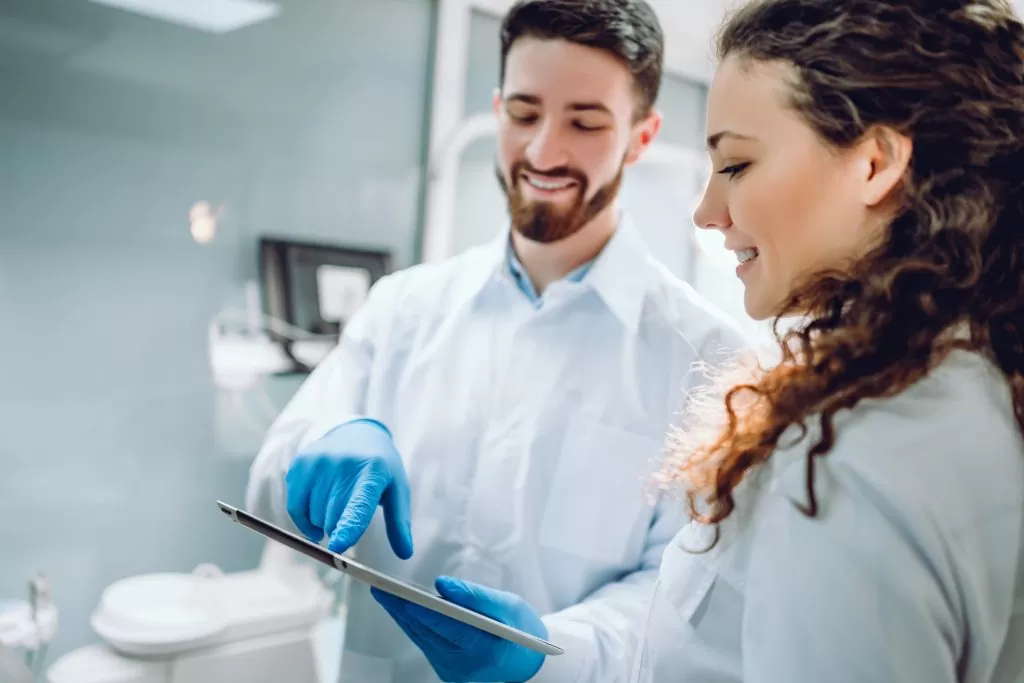 People, medicine, stomatology and health care concept happy male dentist showing tablet pc computer to woman patient at dental clinic office.
